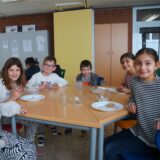 Sechs Kinder sitzen an einem Frühstückstisch und schauen in die Kamera.