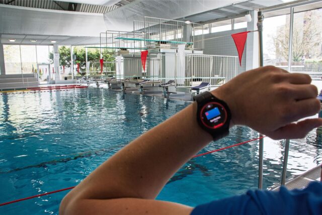 Ein Schwimmmeister in Bochum schaut am Beckenrand auf die Smartwatch an seinem Handgelenk, die ihm anzeigen kann, wenn jemand zu ertrinken droht.