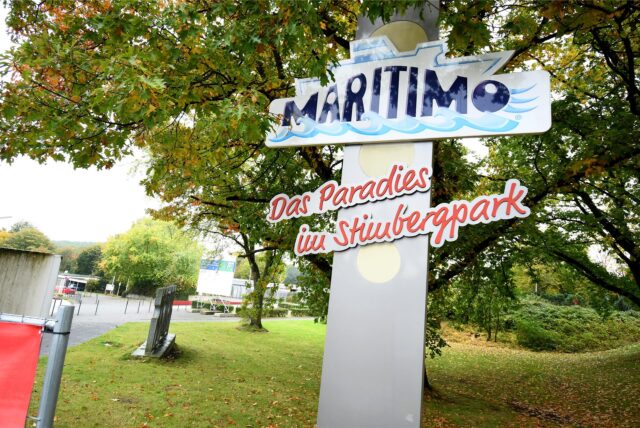 Das Bild zeigt ein Schild, das mit „MARITIMO Das Paradies im Stimbergpark“ beschriftet ist. Das Schild befindet sich inmitten von Bäumen und Grünflächen.