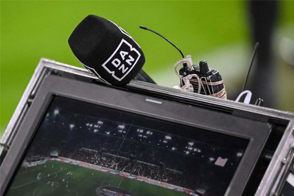 Ein DAZN-Mikrofon liegt während der TV-Übertragung eines Fußballspiels auf einem Monitor. Ein DAZN-Mikrofon liegt während der TV-Übertragung eines Fußballspiels auf einem Monitor.