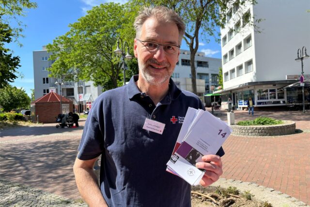 Stefan Arhelger vom Deutschen Roten Kreuz hält Informationsbroschüren zum Thema Schuldnerberatung in die Kamera.