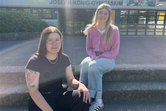 Hannah von Hören und Jule Brinkert sitzen auf den Treppen zum Joseph-König-Gymnasiums in Haltern am See.