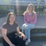 Hannah von Hören und Jule Brinkert sitzen auf den Treppen zum Joseph-König-Gymnasiums in Haltern am See.