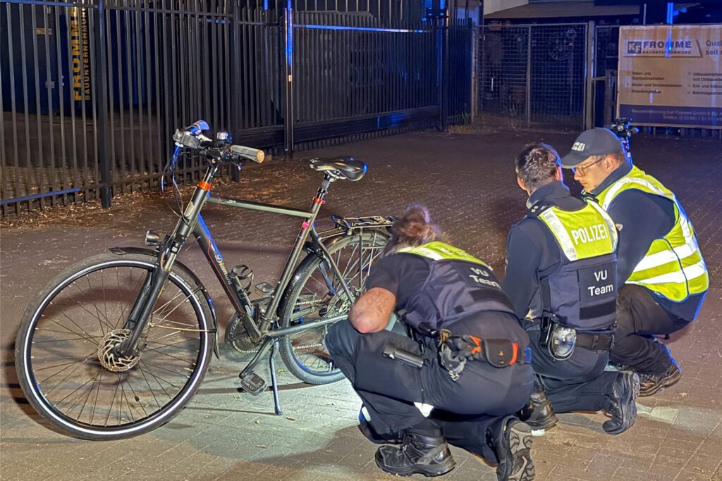 Polizeibeamte knien auf dem Boden und untersuchen vor Ort Spuren. Ein Fahrrad steht neben ihnen. Polizeibeamte knien auf dem Boden und untersuchen vor Ort Spuren. Ein Fahrrad steht neben ihnen.