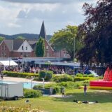 Freibad mit vielen Menschen und aufgebauten Zelten sowie Verkaufsständen und einer Hüpfburg. Grüne Wiese im Vordergrund