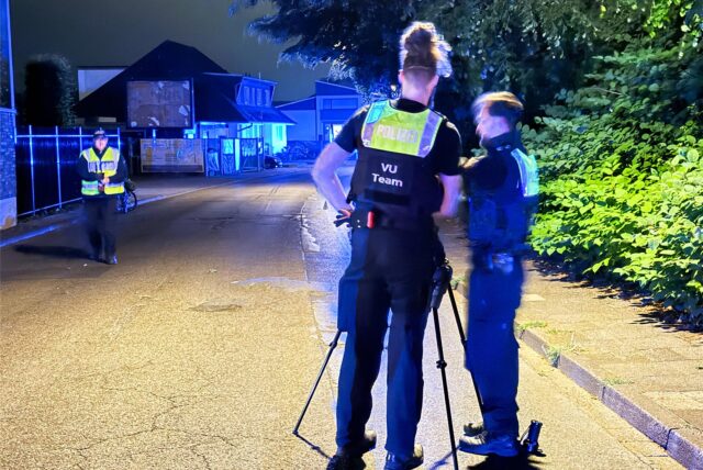 Zwei Beamte des Verkehrsunfall-Teams der Polizei stehen nach dem tödlichen Unfall in Marl, bei dem ein Radfahrer starb, an einer Kamera auf dem Dümmerweg.