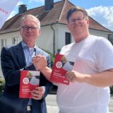 André Dora und Pascal Joswig halten das Wahlprogramm in der Hand und stehen vor der Dattelner Stadthalle.