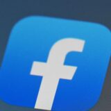 Das Bild zeigt eine Feldansicht mit installierten Metallpfosten, möglicherweise für eine Solaranlage, sowie das Facebook-Logo im Detail.