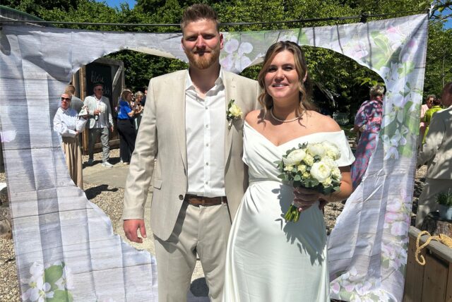 Kevin und Vivien Charizanis stehen an ihrem Hochzeitstag am klein glücklich in Horneburg vor einem Tuch mit herzförmigem Loch.