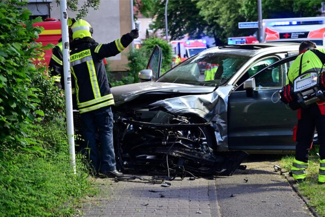 Ein Auto ist gegen ein Schild gefahren, Feuerwehrleute stehen am Wagen.