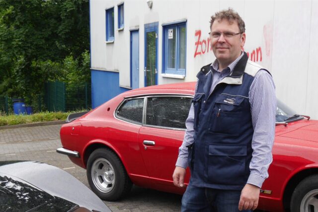 Christian Krispin vom TÜV in Marl hat einige Tipps für Autofahrer. Er steht vor einem roten Auto.