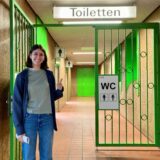 Xenia zeigt Daumen vor dem Eingang zur Toilettenanlage Kampstraße in Dortmund den Daumen hoch.