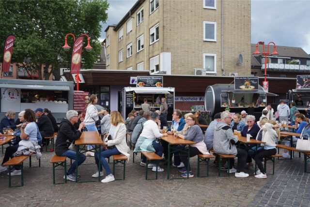Menschen sitzen auf Bänken beim Streetfood-Festival in Datteln.