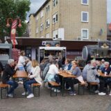 Menschen sitzen auf Bänken beim Streetfood-Festival in Datteln.