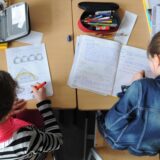 Zwei Grundschülerinnen sitzen im Klassenraum an einem Tisch und arbeiten in ihren Heften.
