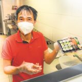 Ein Mann steht hinter einer Theke und hält einen Behälter mit einer Portion Sushi in der Hand.