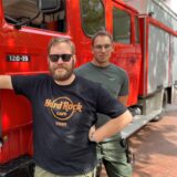 Tim Stracke und Eric Wessendorf stehen neben einem Feuerwehr-Oldtimer.