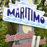 Das Bild zeigt im Vordergrund das Logo des Maritimos und im Hintergrund die Facebook-App auf einem Smartphone.