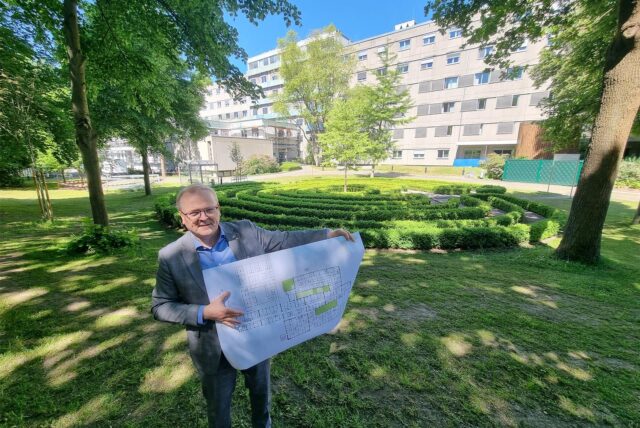 Ein Mann steht im Garten des St. Vincenz und präsentiert einen Bauplan.