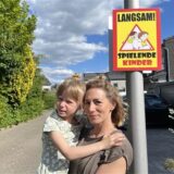 Sophie De Manos, Anwohnerin der Ulrichstraße in Datteln-Horneburg, mit ihrer Tochter Yuna auf dem Arm. Daneben hängt ein Schild: „Langsam! Spielende Kinder“.