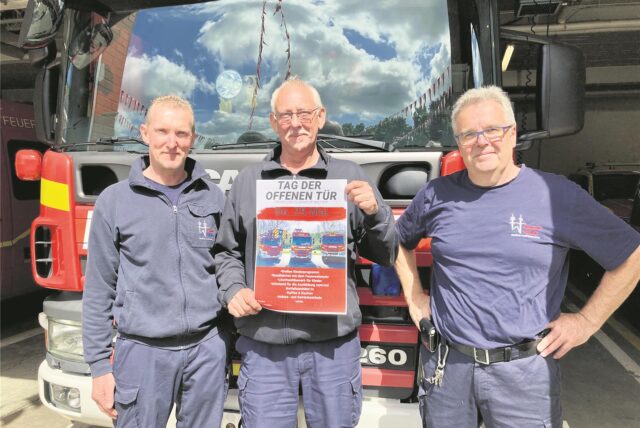 Drei Männer mit Plakat vor einem Feuerwehrauto.