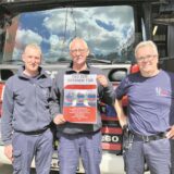Drei Männer mit Plakat vor einem Feuerwehrauto.