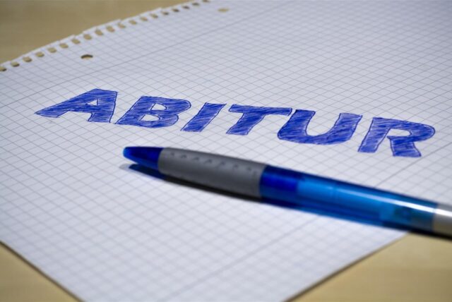 Ein Kugelschreiber liegt auf einem karierten Blatt Papier. Darauf steht das Wort „Abitur“.