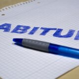 Ein Kugelschreiber liegt auf einem karierten Blatt Papier. Darauf steht das Wort „Abitur“.