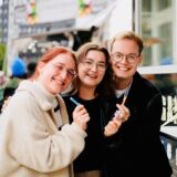 Drei Menschen stehen vor einem Foodtruck und lächeln.