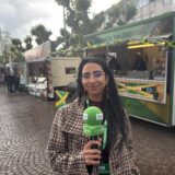 Rosi Taslima Azam steht mit grünem Mikrofon auf dem Rathausplatz in Recklinghausen. Dahinter sind Food-Trucks zu sehen.
