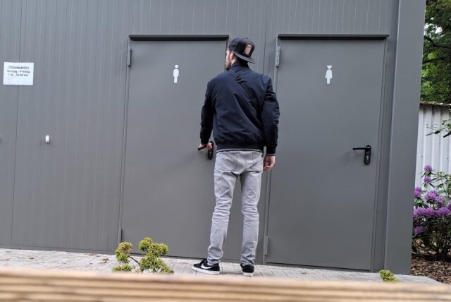 Ein Mann steht vor der verschlossenen WC-Anlage auf dem Friedhof.