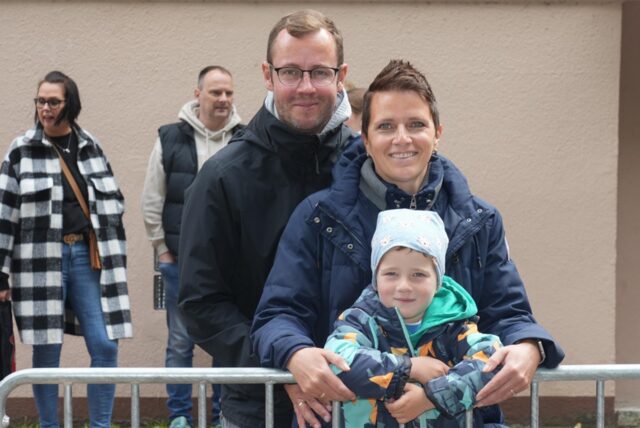 Eine Familie steht an einem Absperrgitter und lächelt in die Kamera.