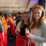 Zwei Frauen mit einem Cocktail in der Hand auf einem Schiff. Sie schauen in die Kamera und lachen.