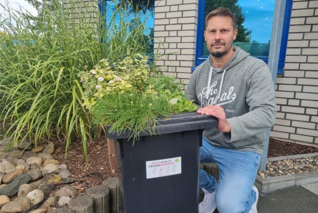 Ein Mann hockt neben einer Biotonne.