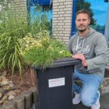 Ein Mann hockt neben einer Biotonne.