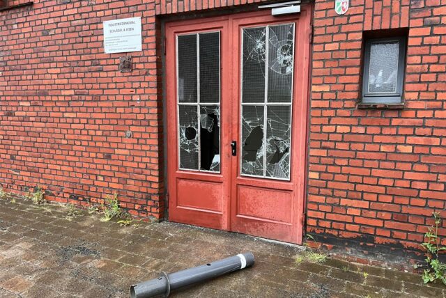 Ein Poller liegt vor einer Doppeltür mit eingeschlagenen Scheiben.