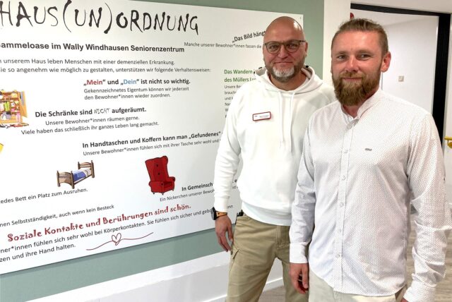 Björn Przybysz (l., Einrichtungsleitung) und Rafael Kus (Pflegedienstleitung) stehen im Wally-Windhausen-Seniorenzentrum in Herten in der dritten Etage, der Gammel-Oase, vor einer großen-Info-Tafel, der Haus(un)ordnung.
