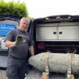 Ein Mann steht an einer alten Weltkriegsbombe und hält einen Zünder in der Hand.