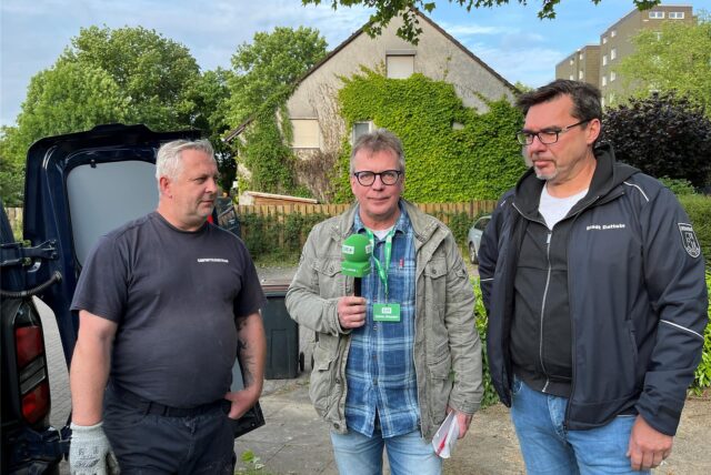 Zwei Männer stehen vor der Kamera. Im Hintergrund ist ein Polizeiauto zu sehen.