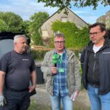 Zwei Männer stehen vor der Kamera. Im Hintergrund ist ein Polizeiauto zu sehen.