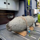 Im Laderaum eines Fahrzeugs liegt eine Weltkriegsbombe. Die Bombe ist mit Gurten gesichert und wird von Holzblöcken stabilisiert.