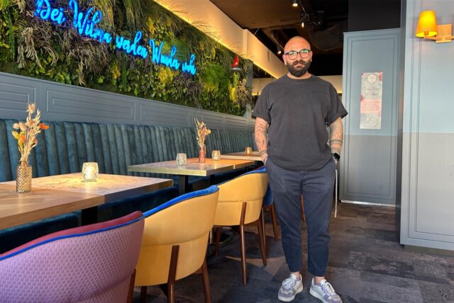 Can Korkmaz, ein Mann mit Bart und Brille, steht in seinem Restaurant.