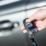 Eine Person hält einen Autoschlüssel in der Hand. Im Hintergrund ist eine Autotür zu sehen.