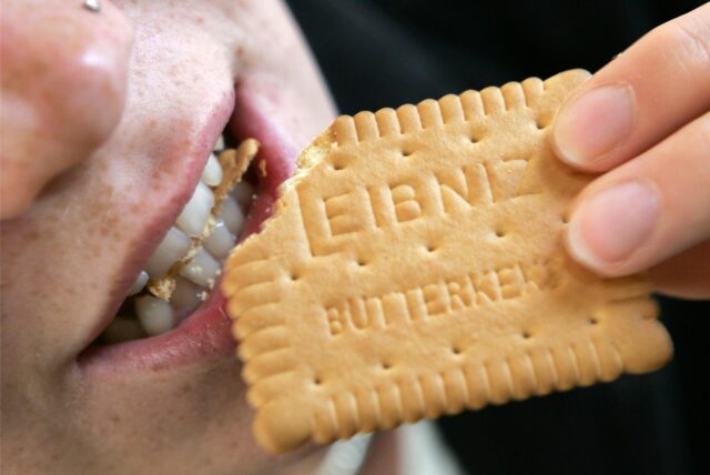 Eine Frau beißt in einen Leibniz-Butterkeks.