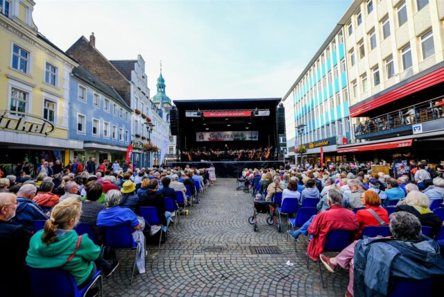 Besucher sitzen in Recklinghausen bei dem Open-Air-Konzert der NPW auf dem Altstadtmarkt