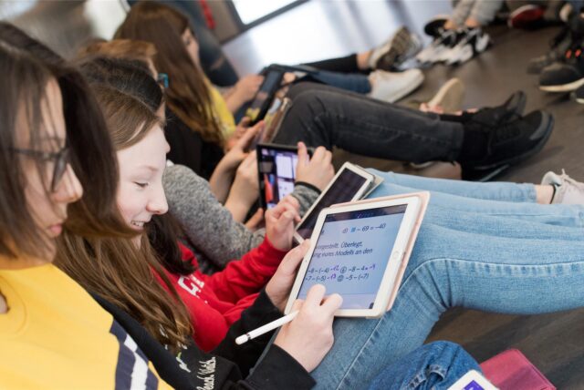 Einige Schülerinnen haben ein iPad auf den Knien. Sie bearbeiten Mathematik-Aufgaben.
