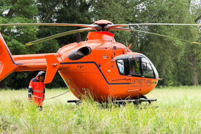Ein roter Rettungshubschrauber steht auf einer Wiese, daneben steht eine Person in Fliegerkluft.
