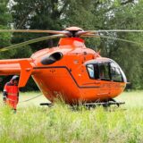 Ein roter Rettungshubschrauber steht auf einer Wiese, daneben steht eine Person in Fliegerkluft.