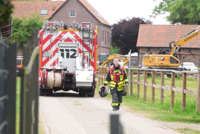 Ein Fahrzeug der Feuerwehr steht auf dem Gelände eines landwirtschaftlichen Betriebes in Gladbeck. Im Vordergrund geht ein Feuerwehrmann in voller Montur über einen gepflasterten Weg.