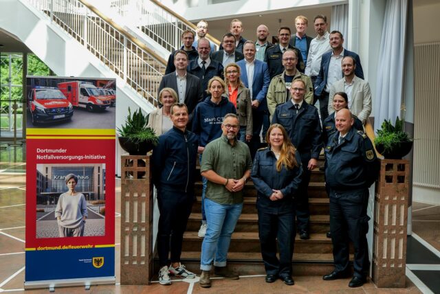 Im Dortmunder Rathaus hat die Auftaktveranstaltung eines neuen Notfallversorgungs-Projekts der Feuerwehr stattgefunden. Die Teilnehmer stehen auf einer Treppe im Eingangsbereich des Rathauses.